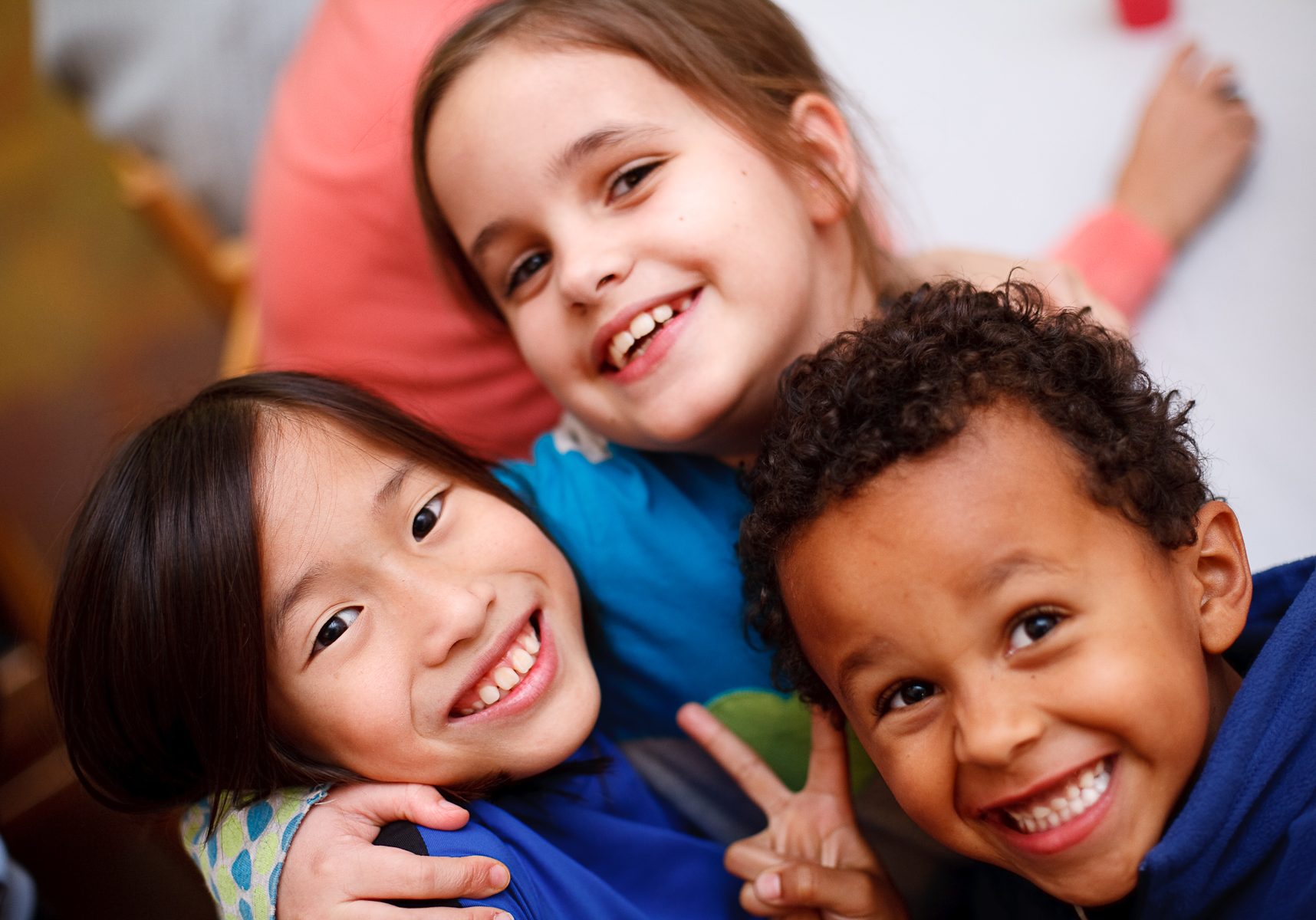 Corporate Photo, two smiling girls and one smiling boy looking up at the camera while they are hugging each other.